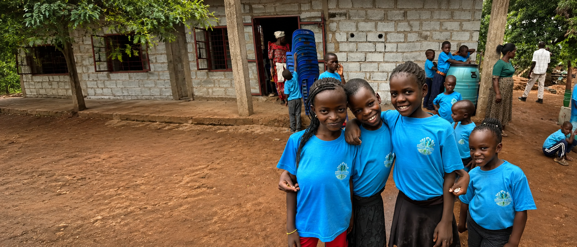 Children in blue Roots of Mercy shirts standing together outside their school in Uganda